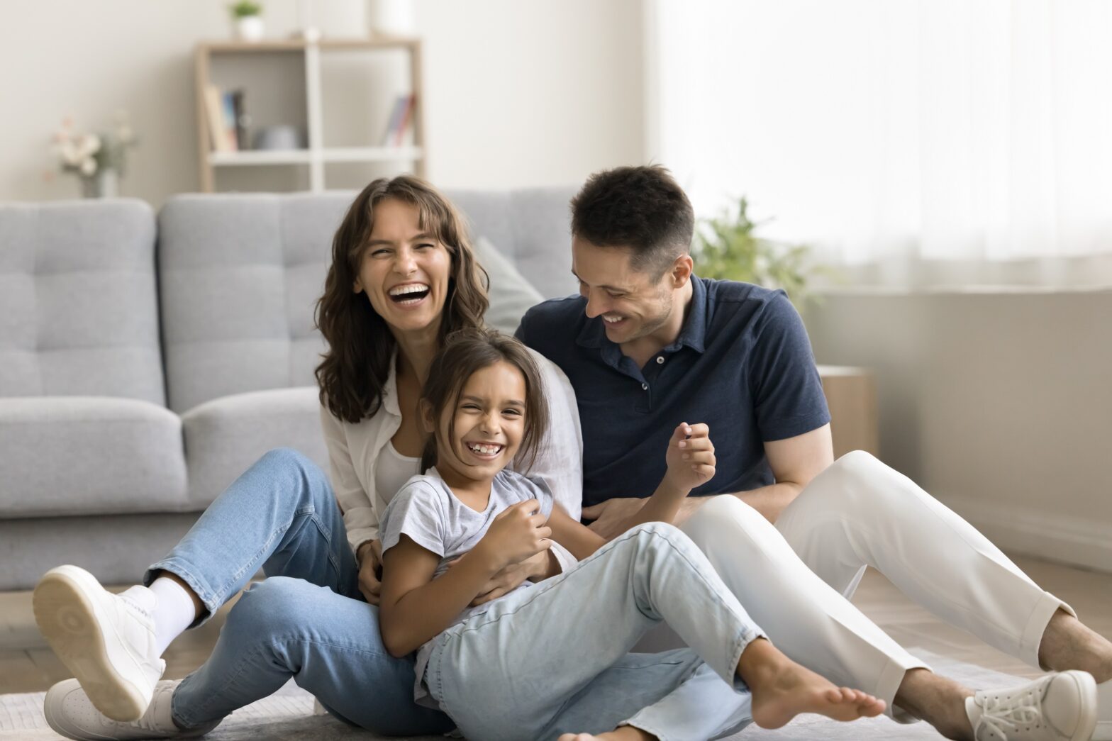 Familie sitzt im Wohnzimmer auf Fußboden und lacht